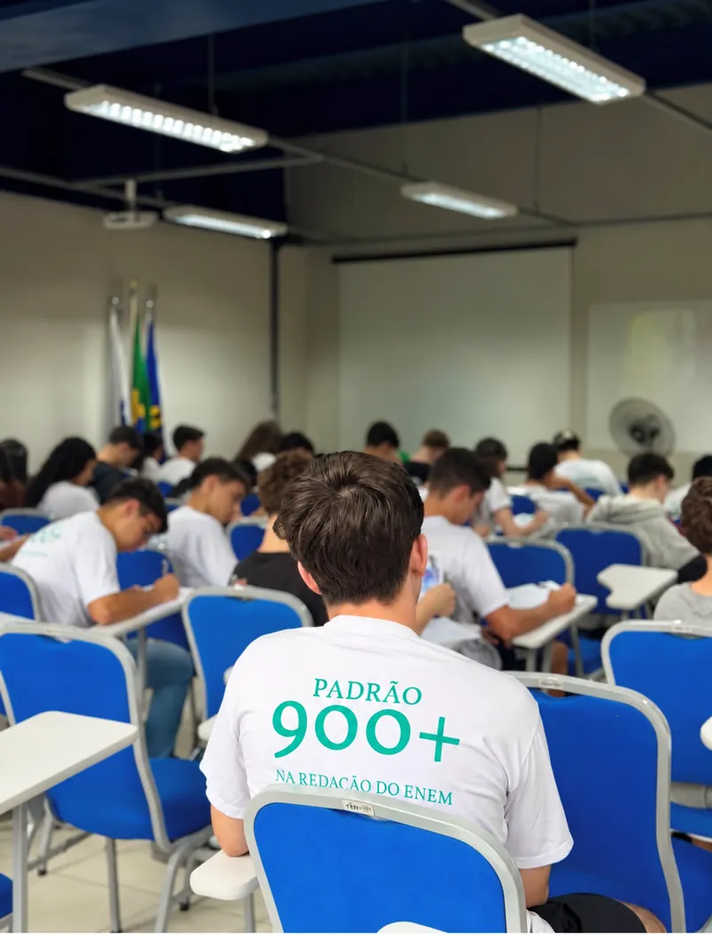 Alunos fazendo simulado; um deles veste a camiseta 'Padrão 900+ na redação do ENEM'